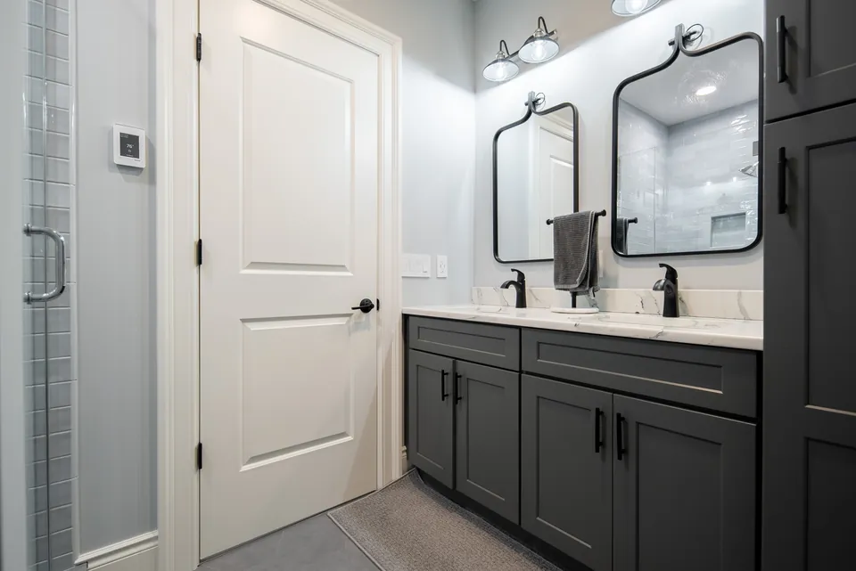 Bathroom with a charcoal double vanity, two black-framed mirrors and a glass-door tile shower