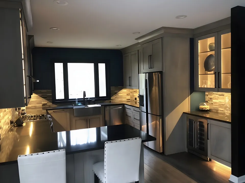 Kitchen remodel with dark gray shaker cabinets, black countertops, a glass tile backsplash and under-cabinet lighting