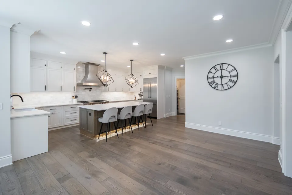 Open-plan kitchen seen from the living area, with wide-plank wood floors and a long island