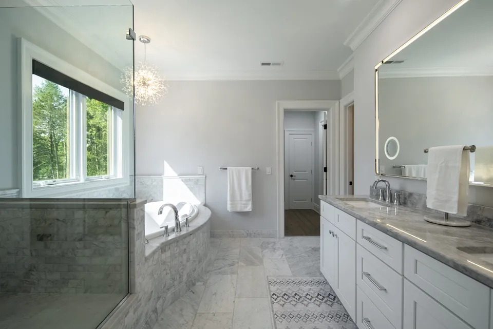 Primary bathroom with a glass shower, a tub set in marble tile under the window and a double vanity