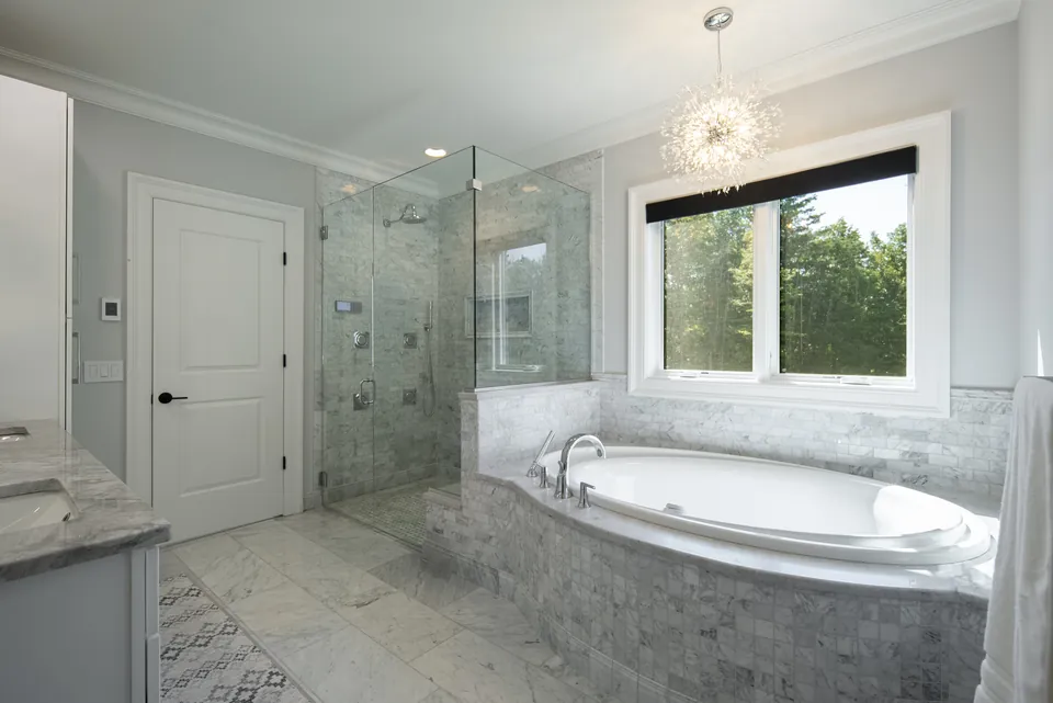 Marble-tiled tub deck and glass shower enclosure in a remodeled primary bathroom