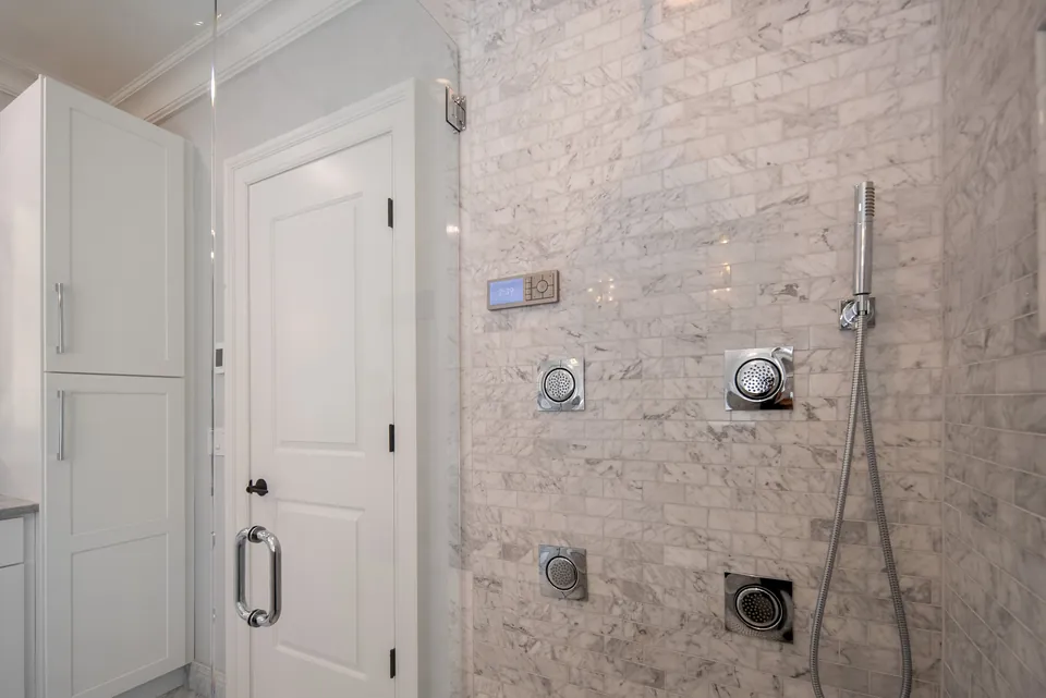 Marble tile shower wall with body sprays, a handheld shower and a digital shower control