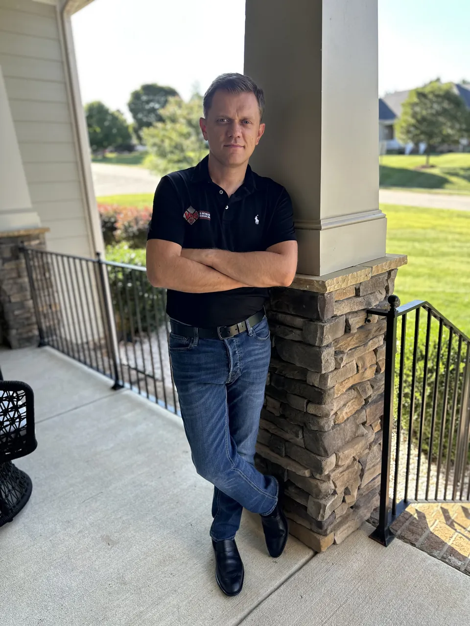 Serge, owner of V&S Tile & Bath, standing on a front porch in a V&S shirt